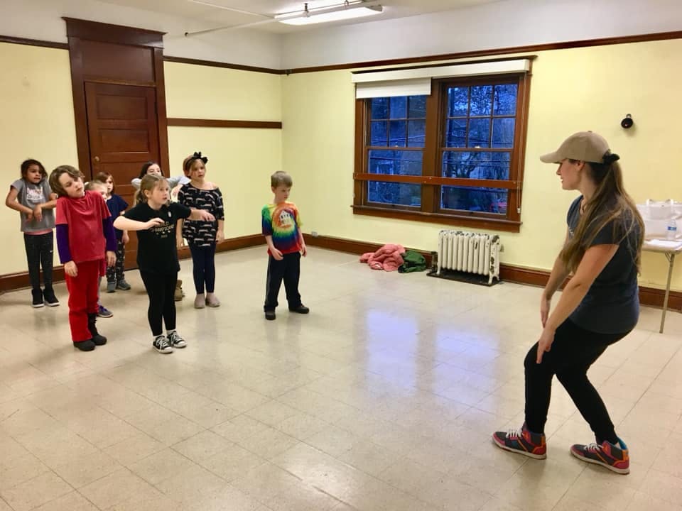 Adult and children in a room, some children watching the adult is facing