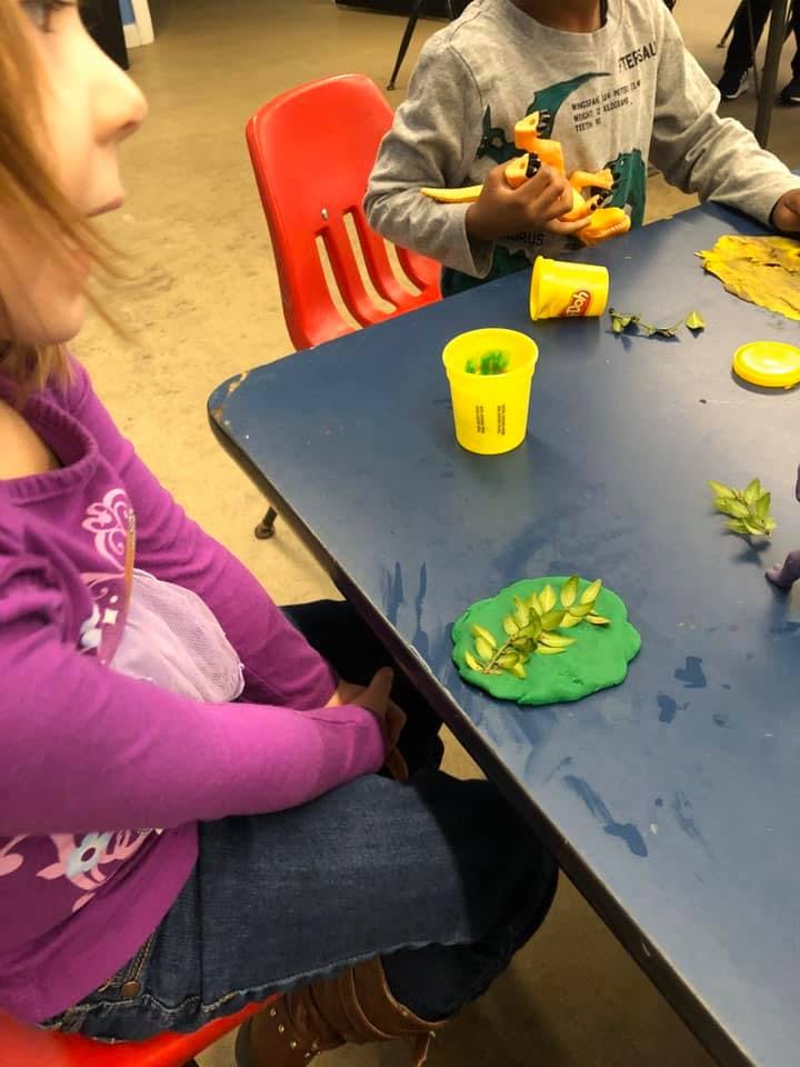 Children playing with modeling clay and toy dinosaurs at a table