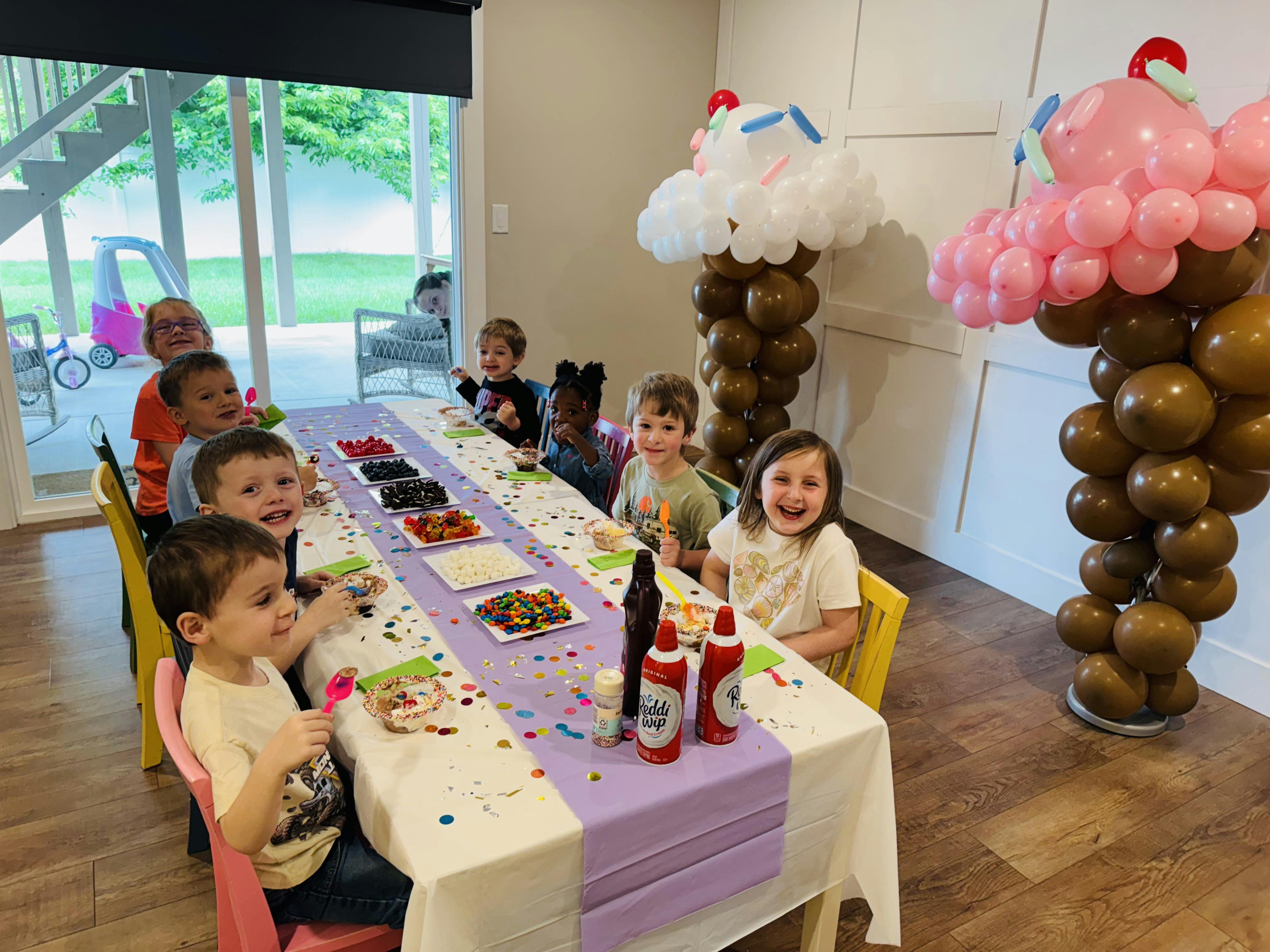 Children sitting at a long table with bowls of toppings for a dessert bar