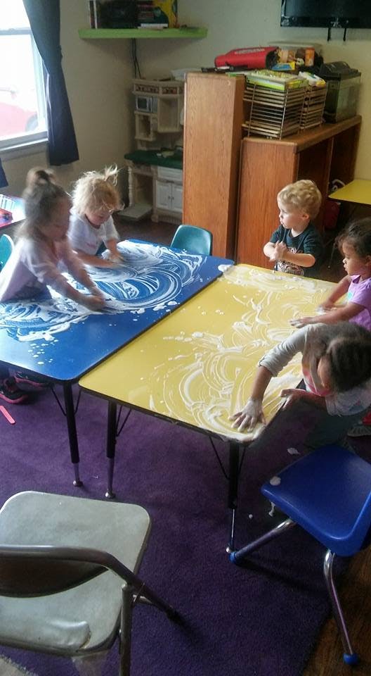 Children playing with white foam on blue and yellow tables in a classroom