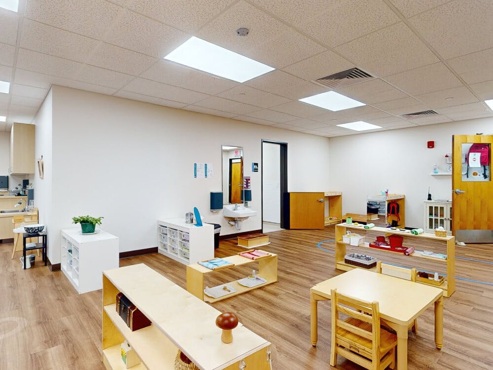An empty classroom with wooden floors and several wooden tables and shelves
