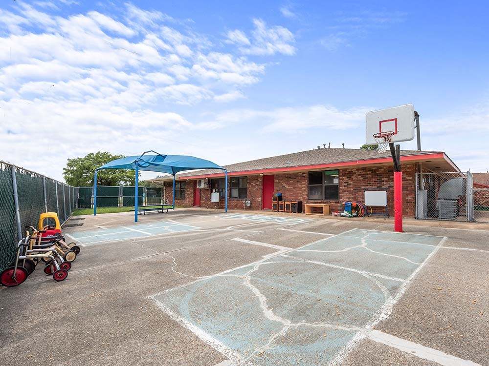 Outdoor play area with a basketball hoop, covered seating, and tricycles