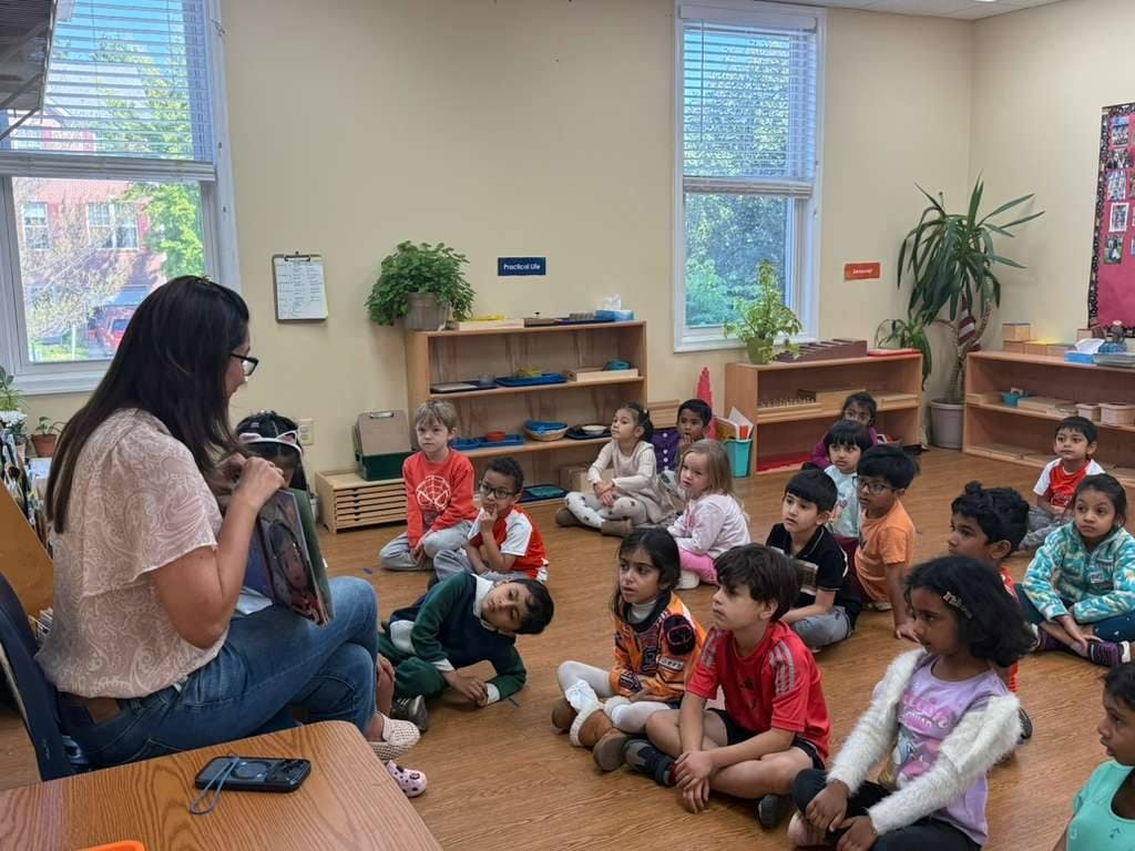 Person sitting on a chair reading a book to a group of children