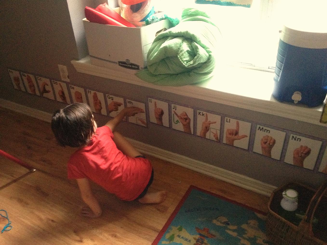 Child on floor reaching for sign language cards on wall