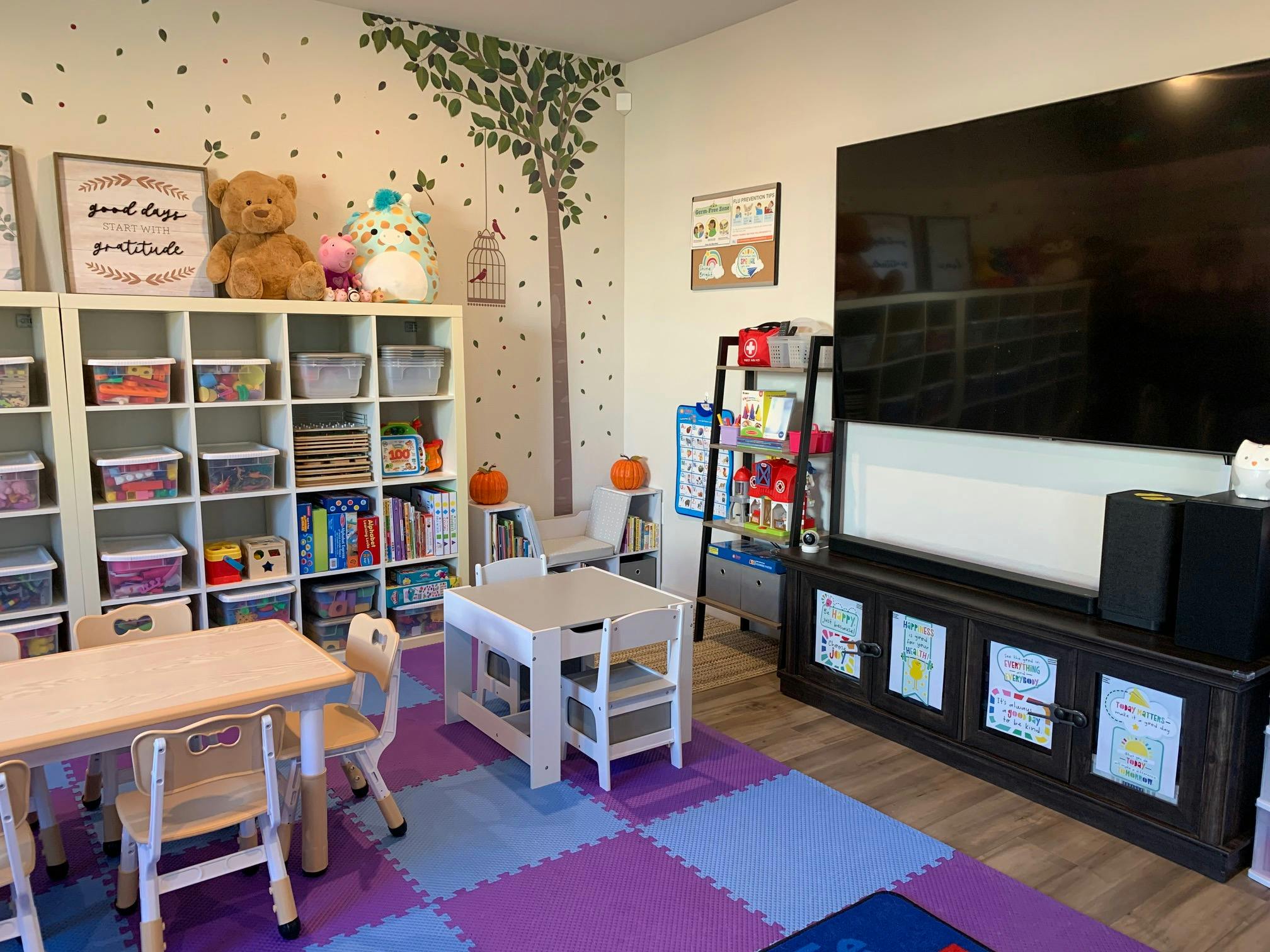 Children's play area with small tables and chairs, shelves with toys, and a large TV