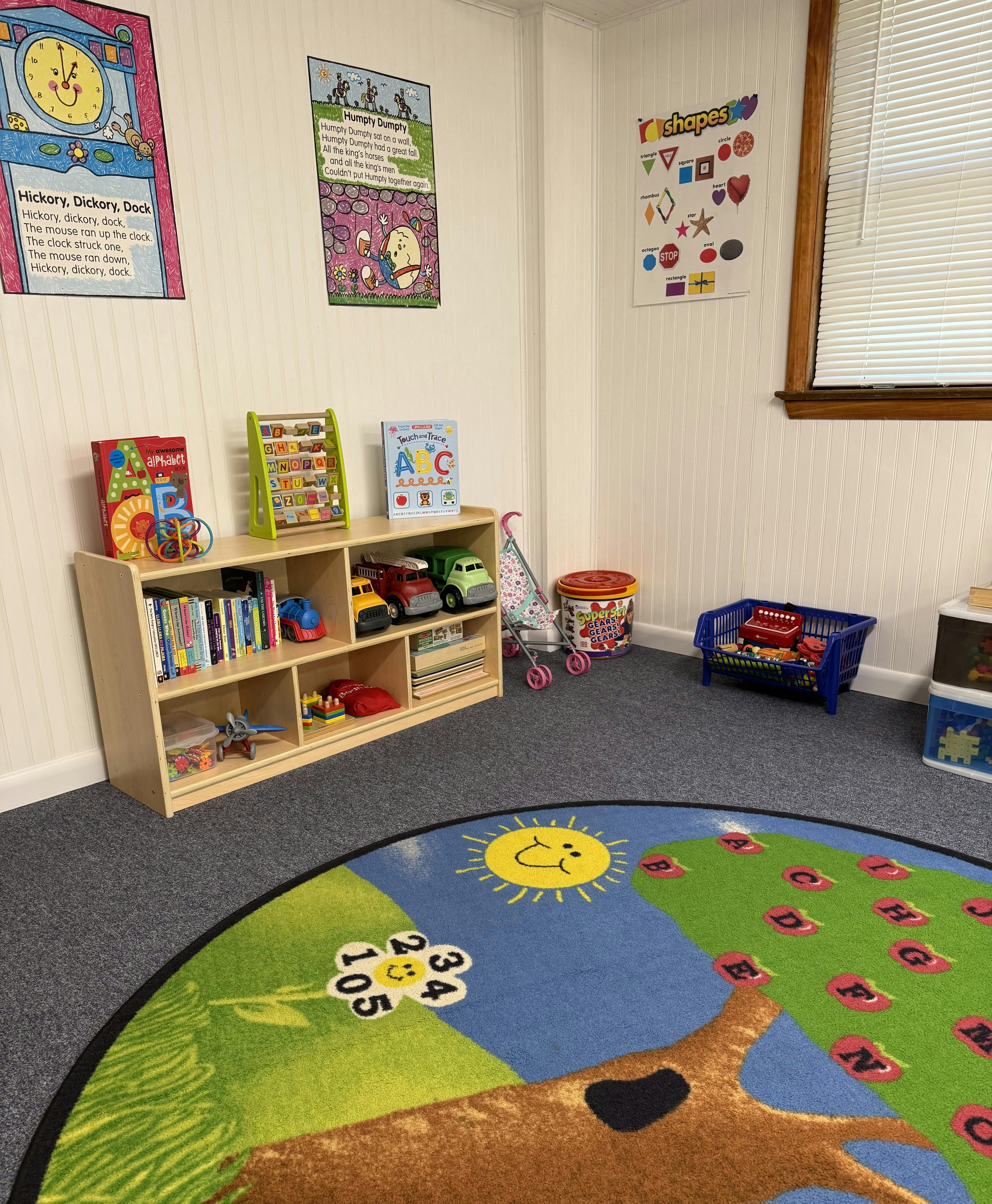 Children's playroom with bookshelf, toys, posters on walls, and an alphabet rug