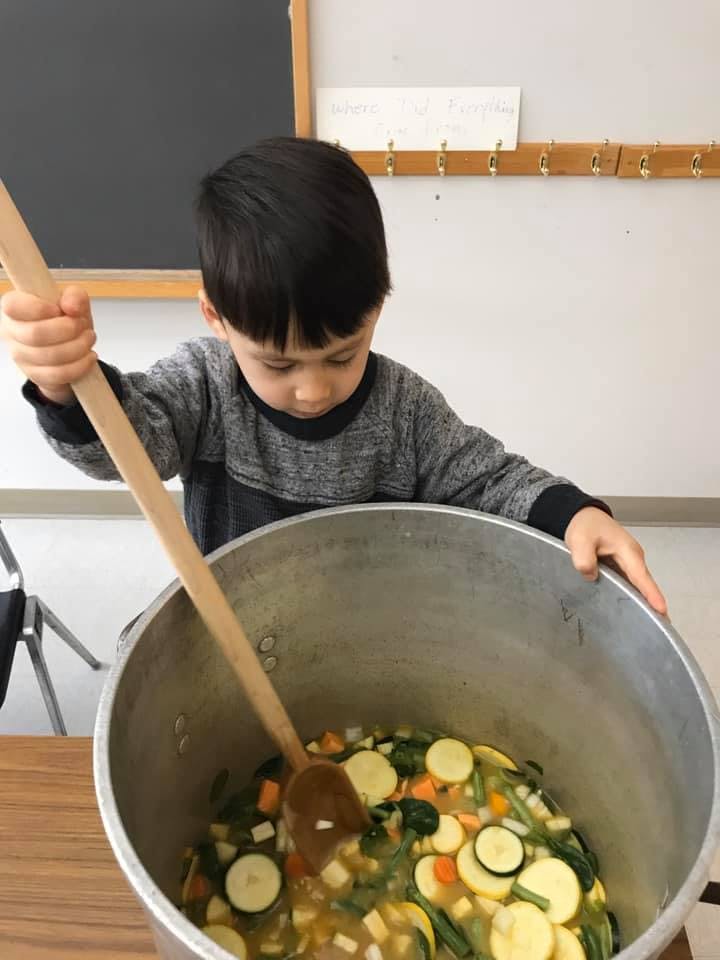 Child stirring a large pot of vegetables with a wooden spoon