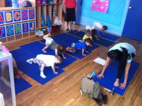 Children and an adult doing yoga poses on blue mats in a room