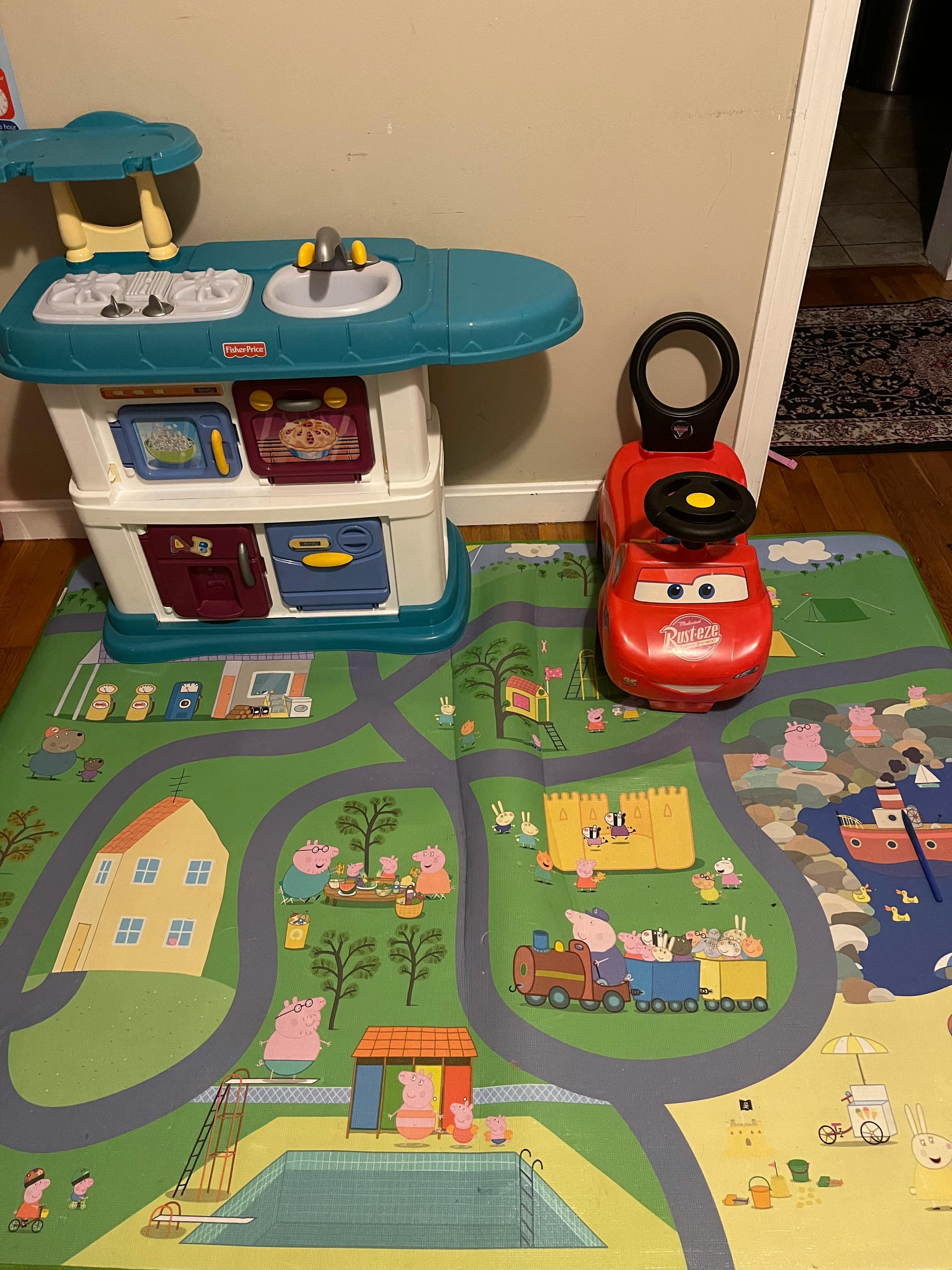 Toy kitchen and red ride-on car on a playmat