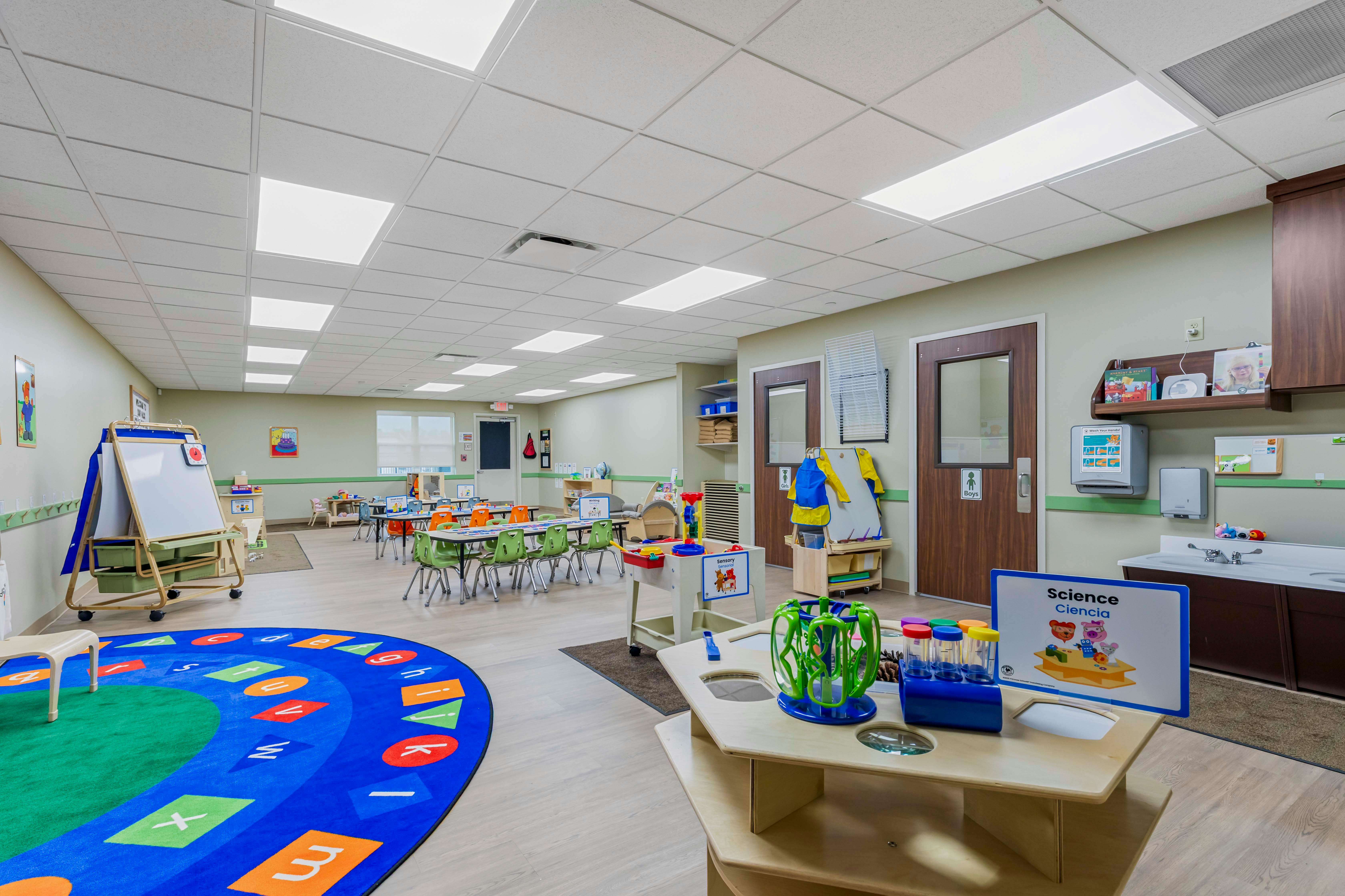 Classroom with tables, chairs, a rug with letters, and activity stations