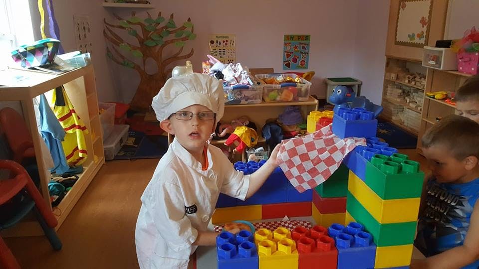 Child in chef's hat and coat playing with large building blocks