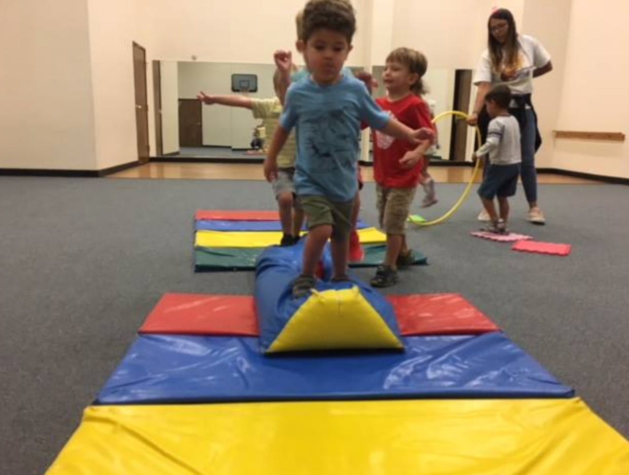 Child balancing on a blue and yellow mat with other children nearby
