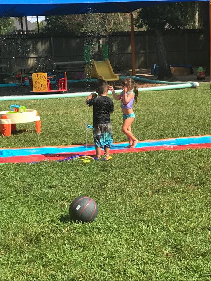 Two children playing with water on a slip and slide in a grassy yard
