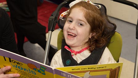 Child in a chair laughing while looking at a book