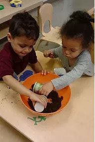 Two children playing with dirt in a bowl