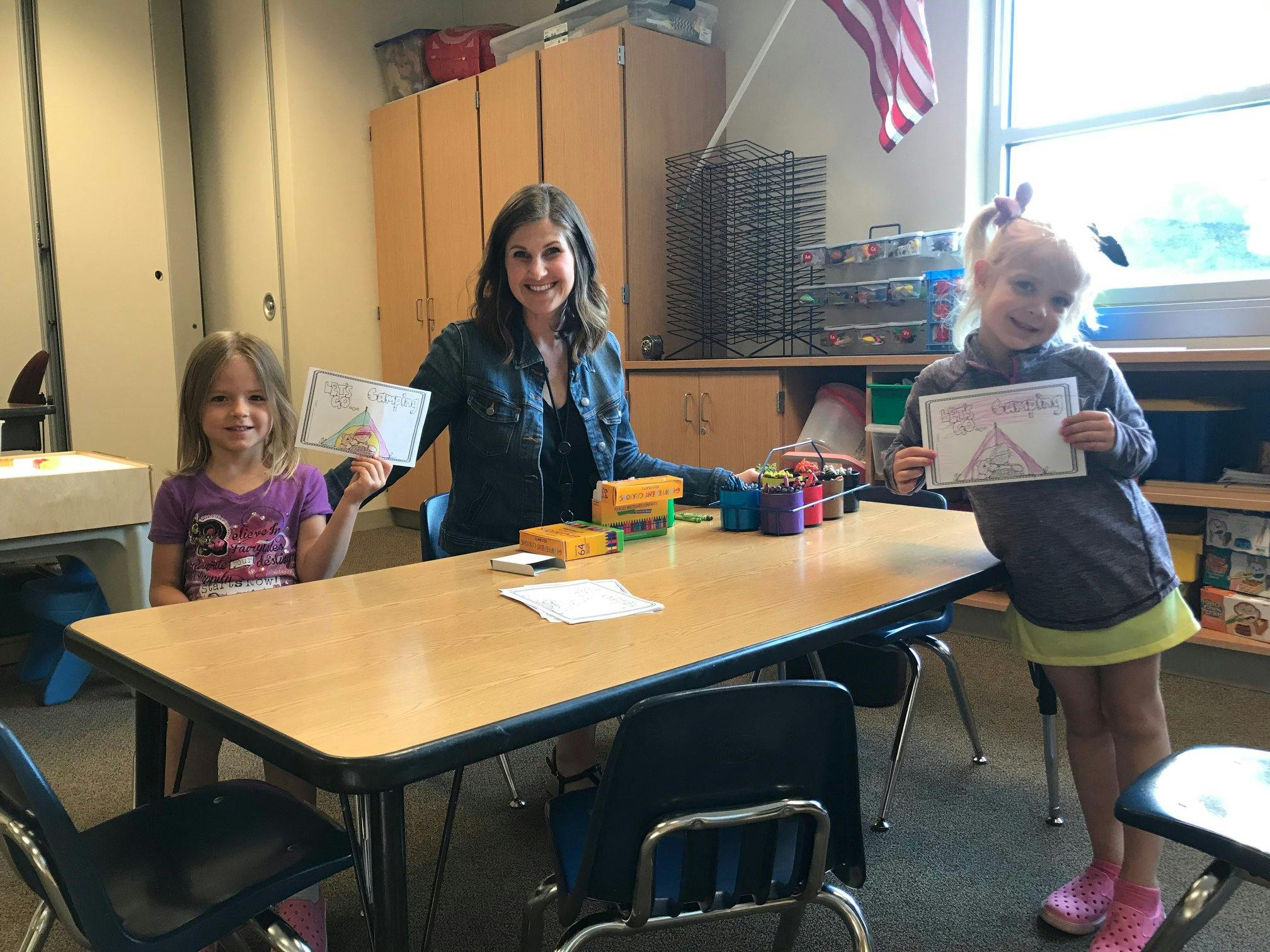 Person and two children holding up certificates in a classroom