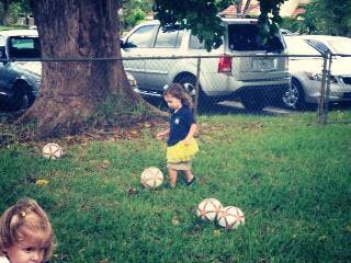 Child playing with multiple soccer balls in a grassy area