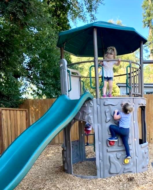 Two children playing on a playground structure with a slide and climbing wall