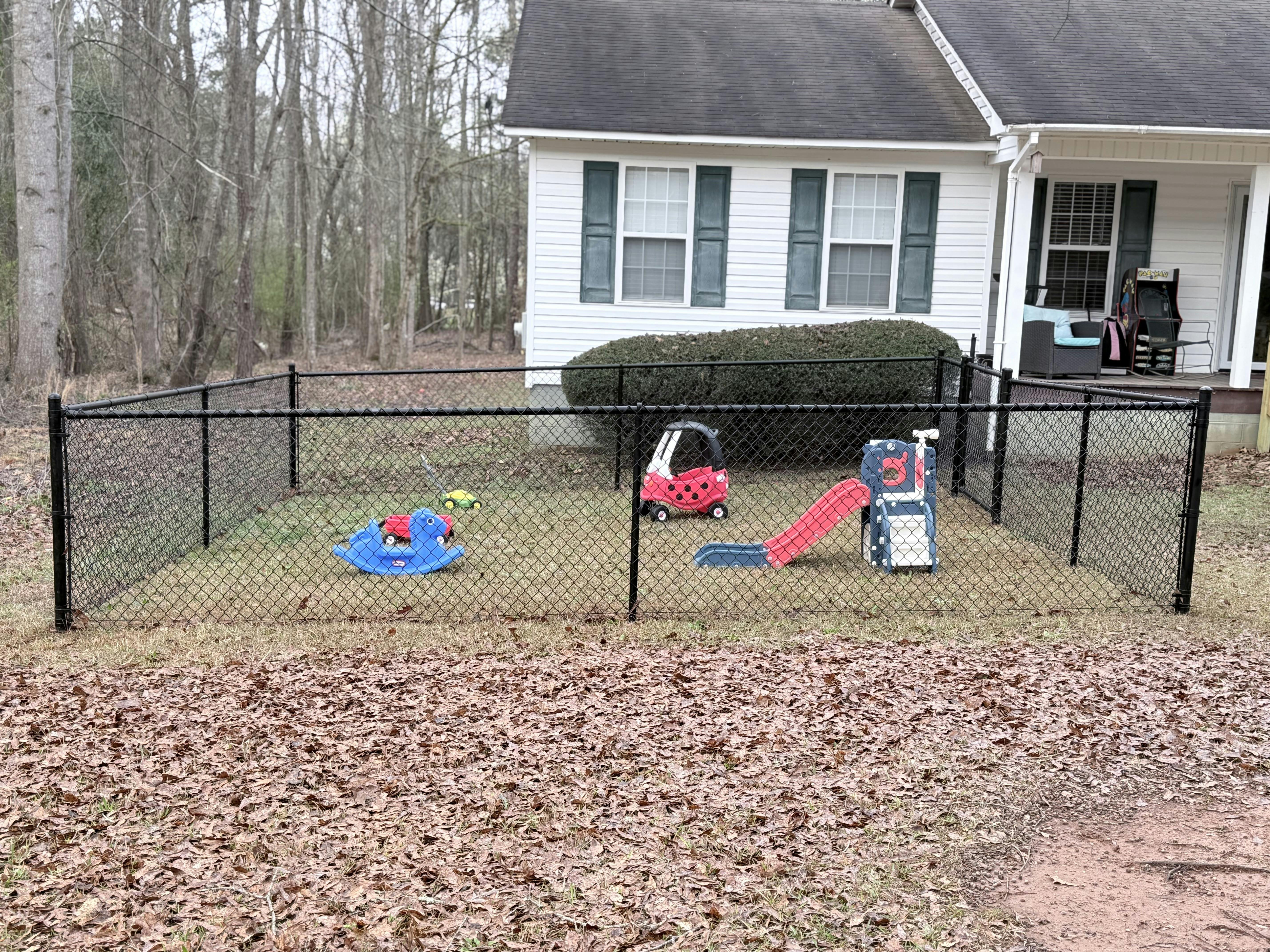 Playground area with small slide, rocking toy, and child's car within a fence