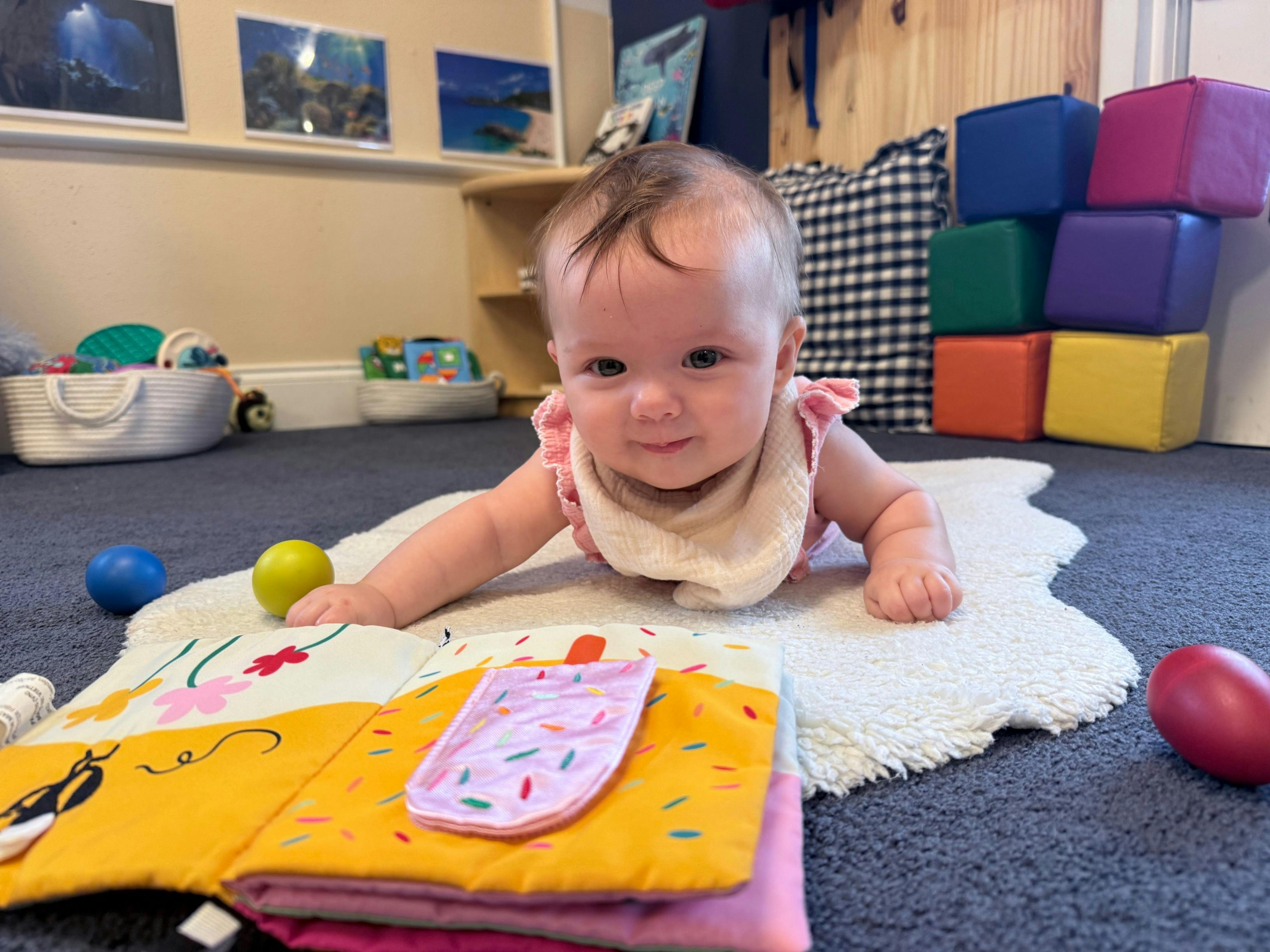 Child on stomach on a rug with a soft book and toys