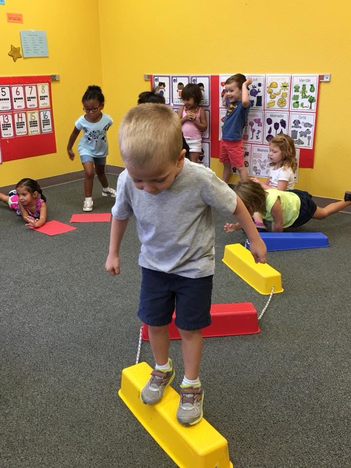 Child walking on yellow balance beam in a classroom with other children