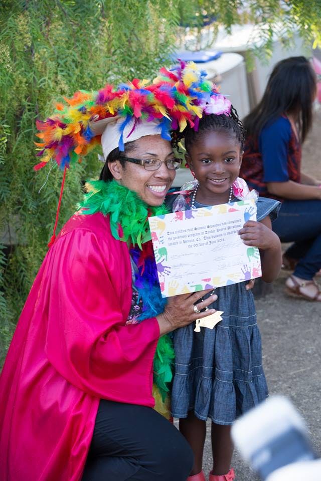 Person in graduation attire with colorful feathers and child holding certificate