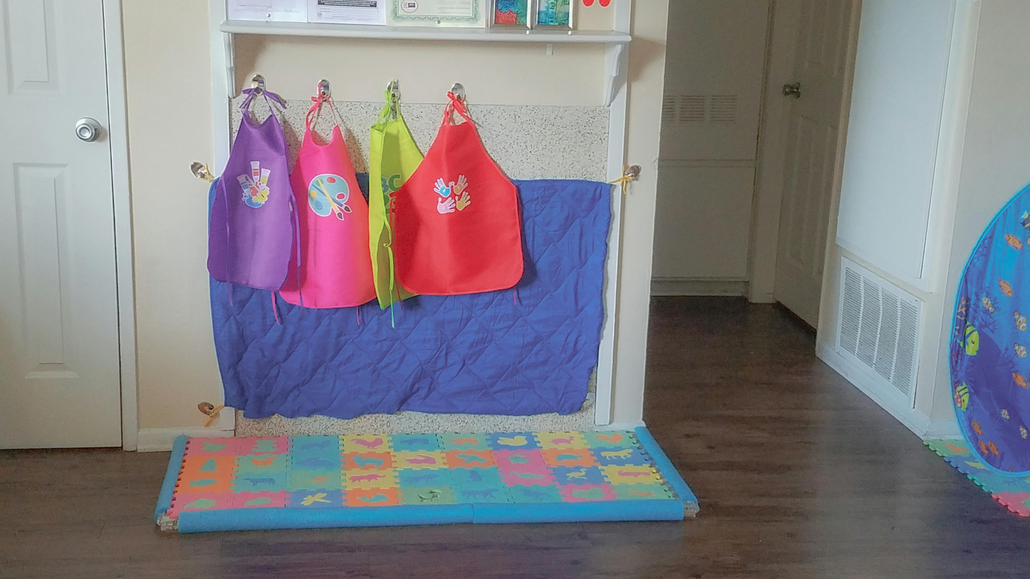 Four aprons hanging on a wall above a colorful playmat