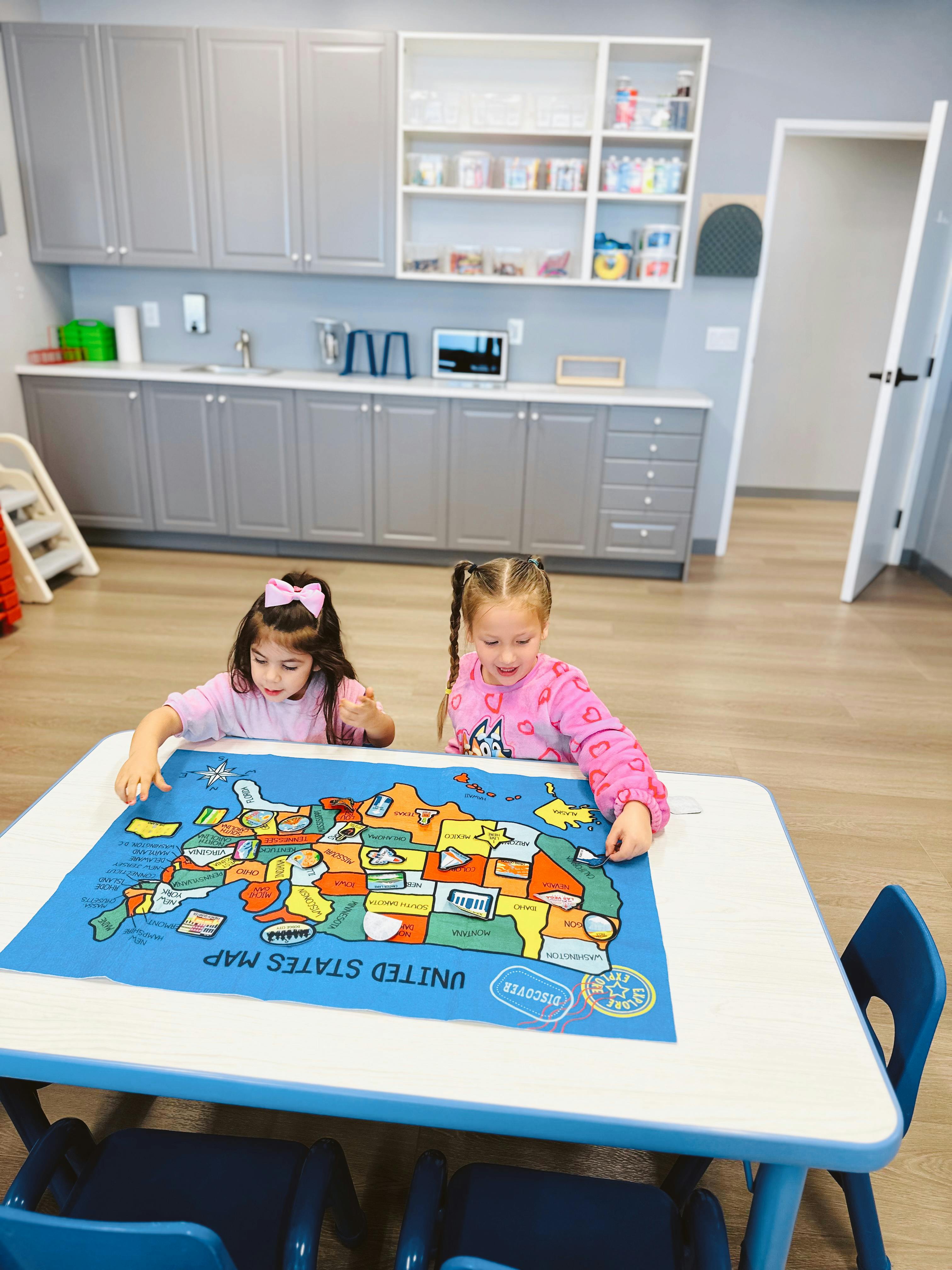 Two children playing with a United States map puzzle at a table