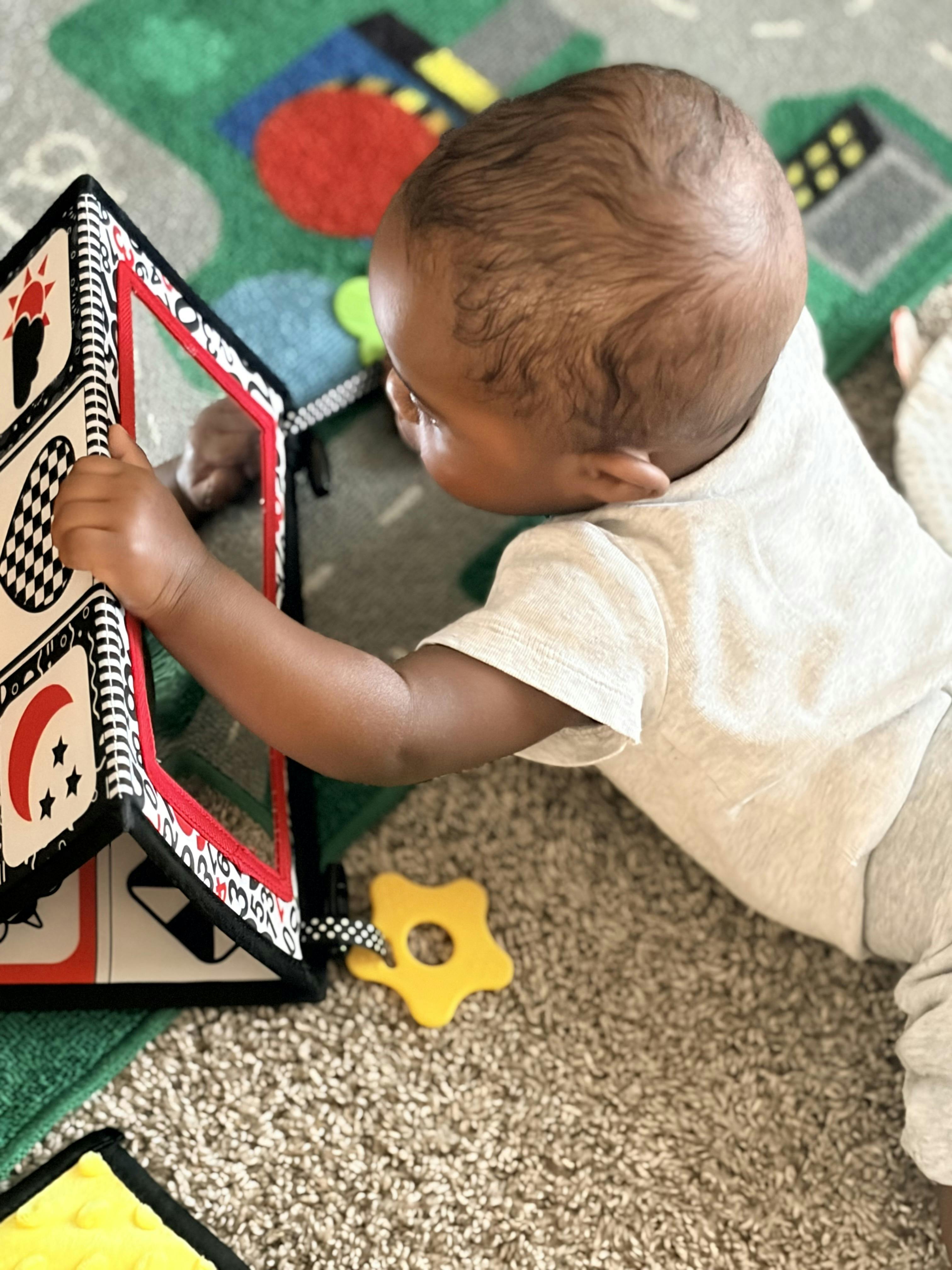 Child lying on a mat and reaching for a sensory mirror toy