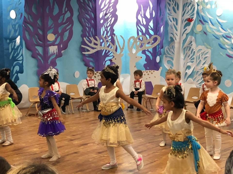 Children in costumes dancing on a stage with a winter-themed backdrop