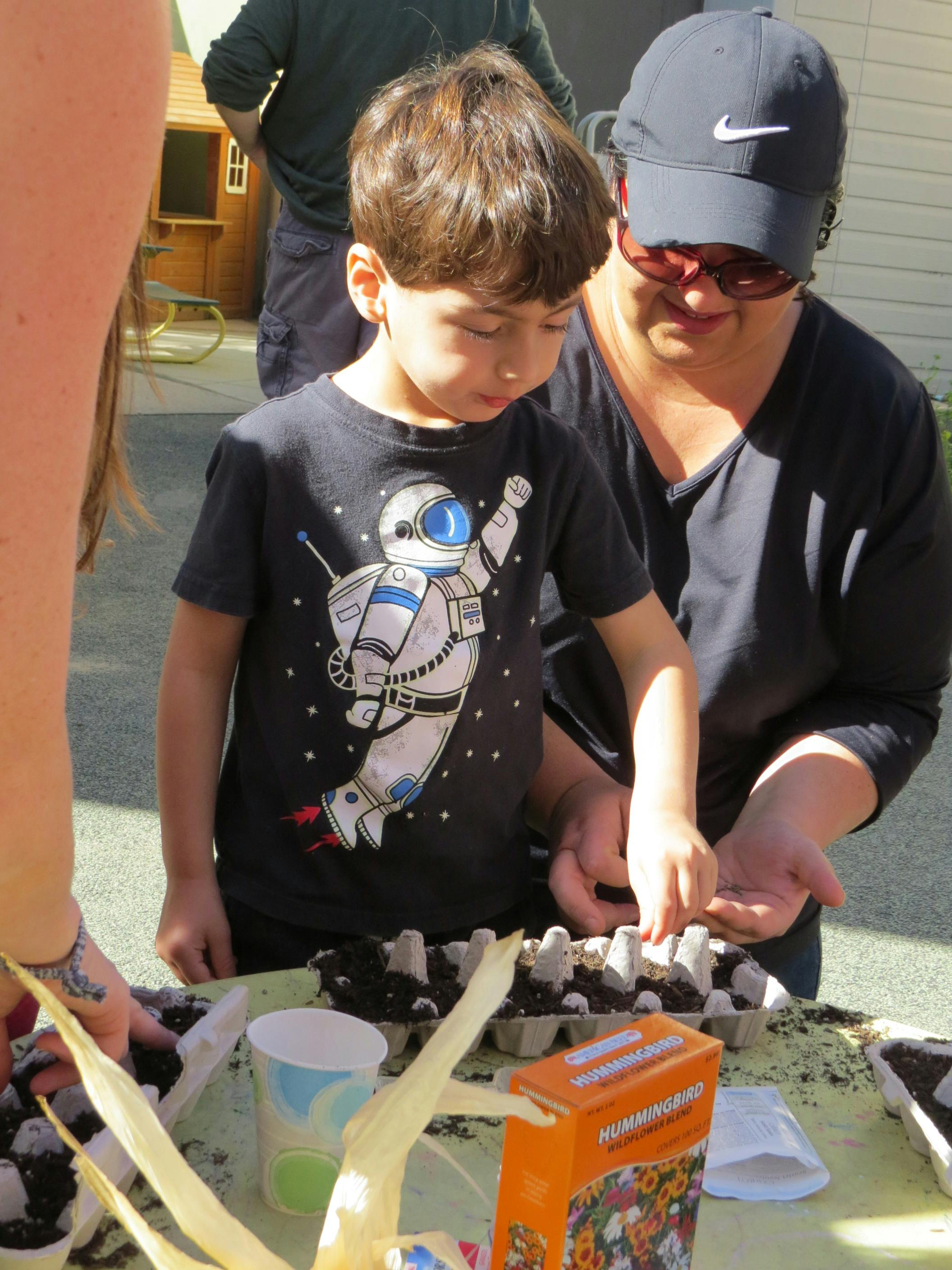 Child and person planting seeds in egg cartons