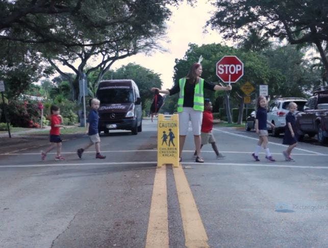 Person in safety vest helping children cross the street