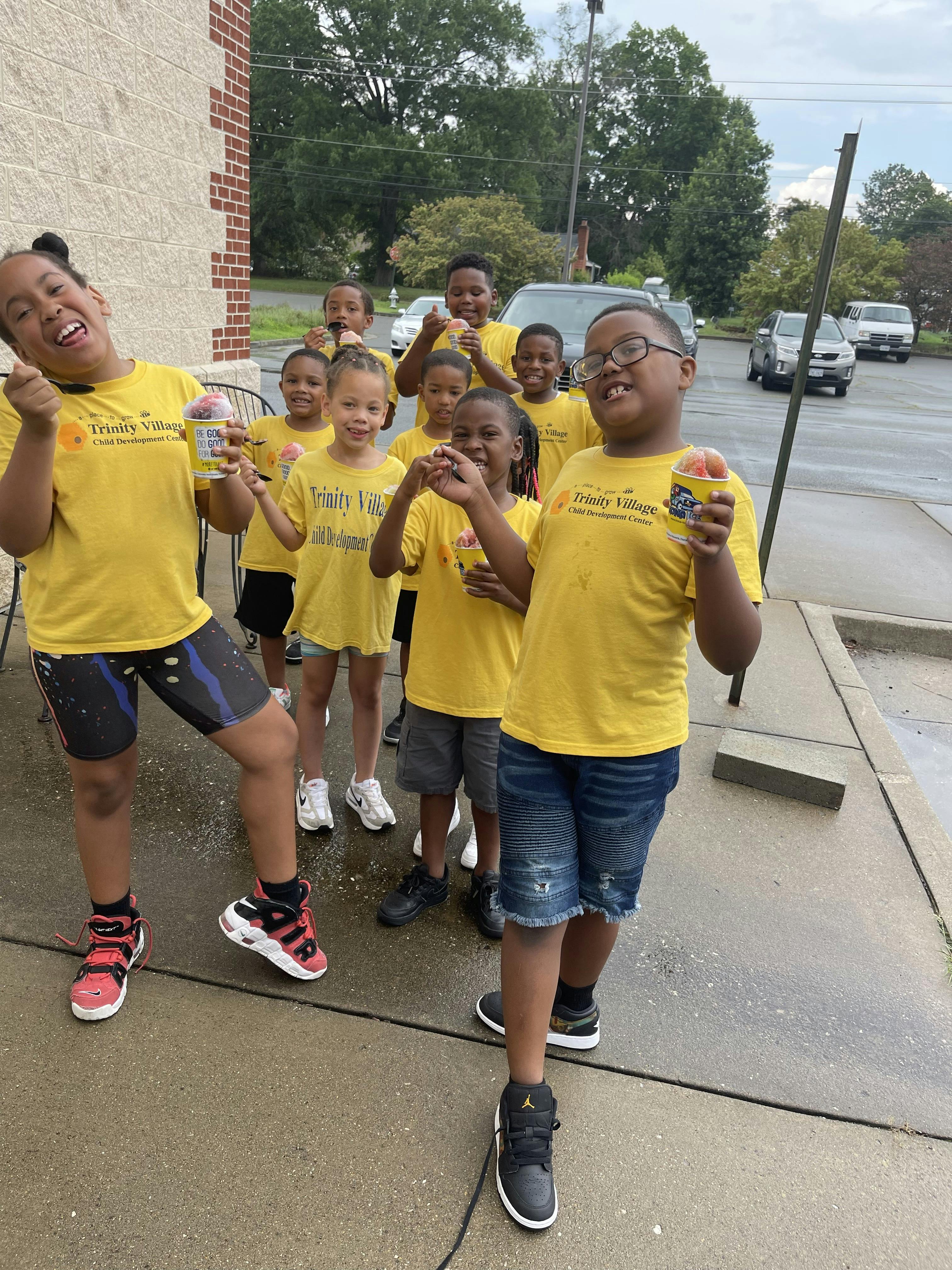 Group of children in yellow shirts eating shaved ice outside