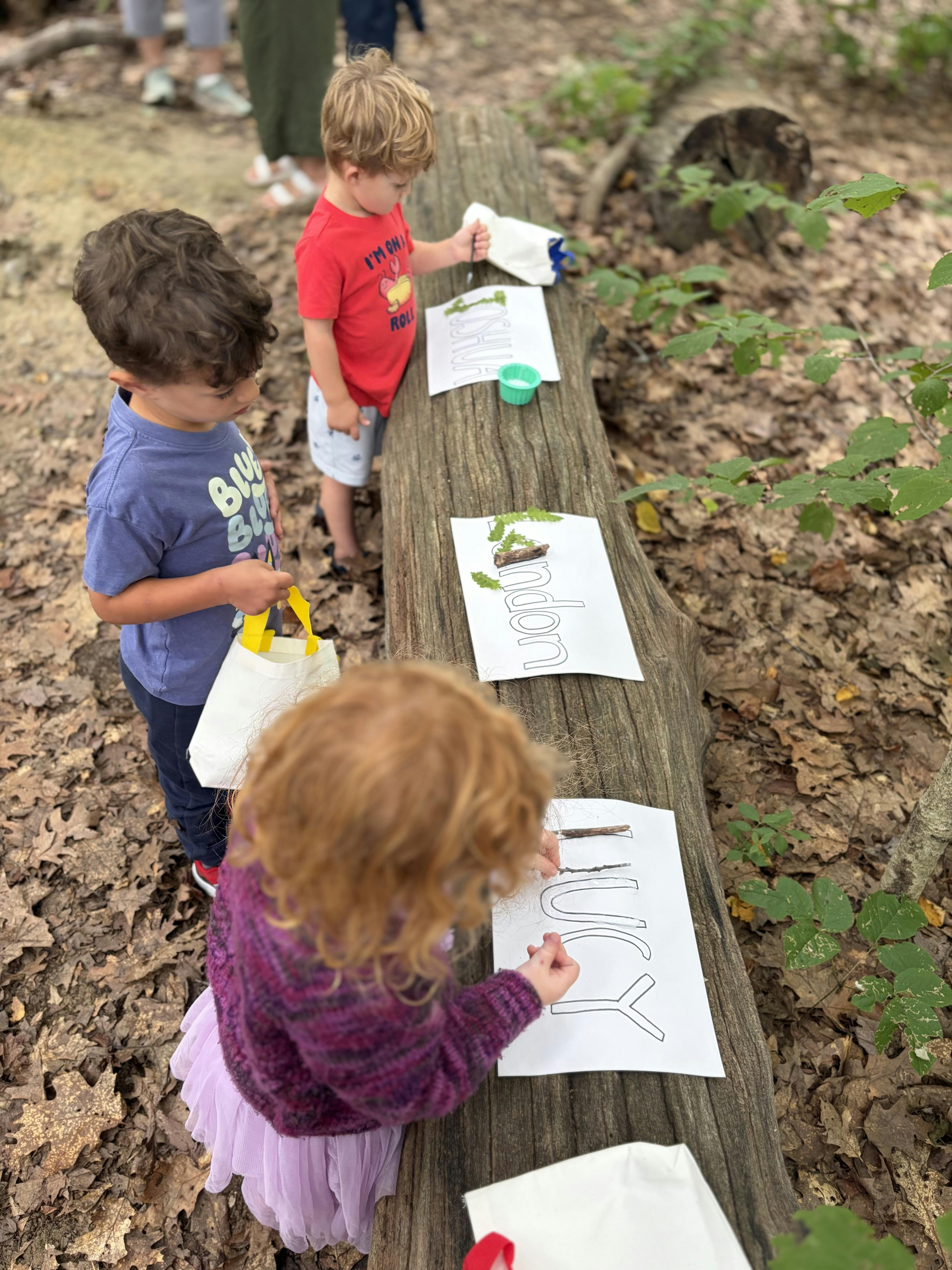 Three children working on craft projects with nature items on a fallen log