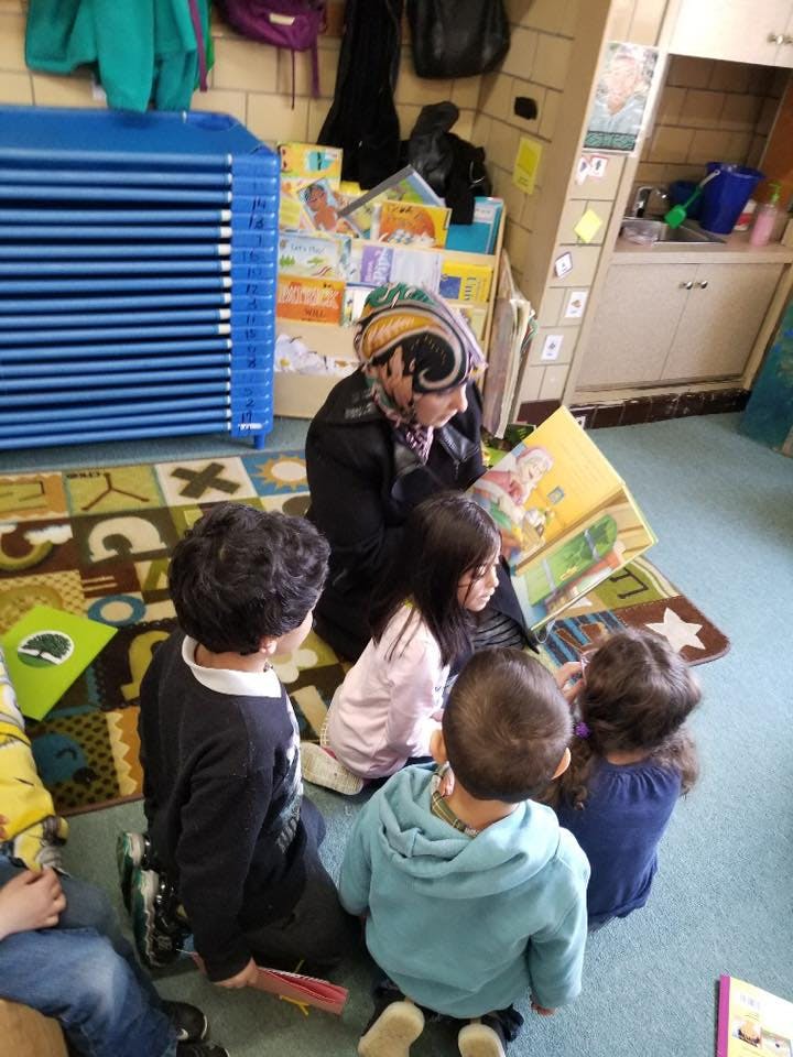 Person reading a book to a group of children in a classroom