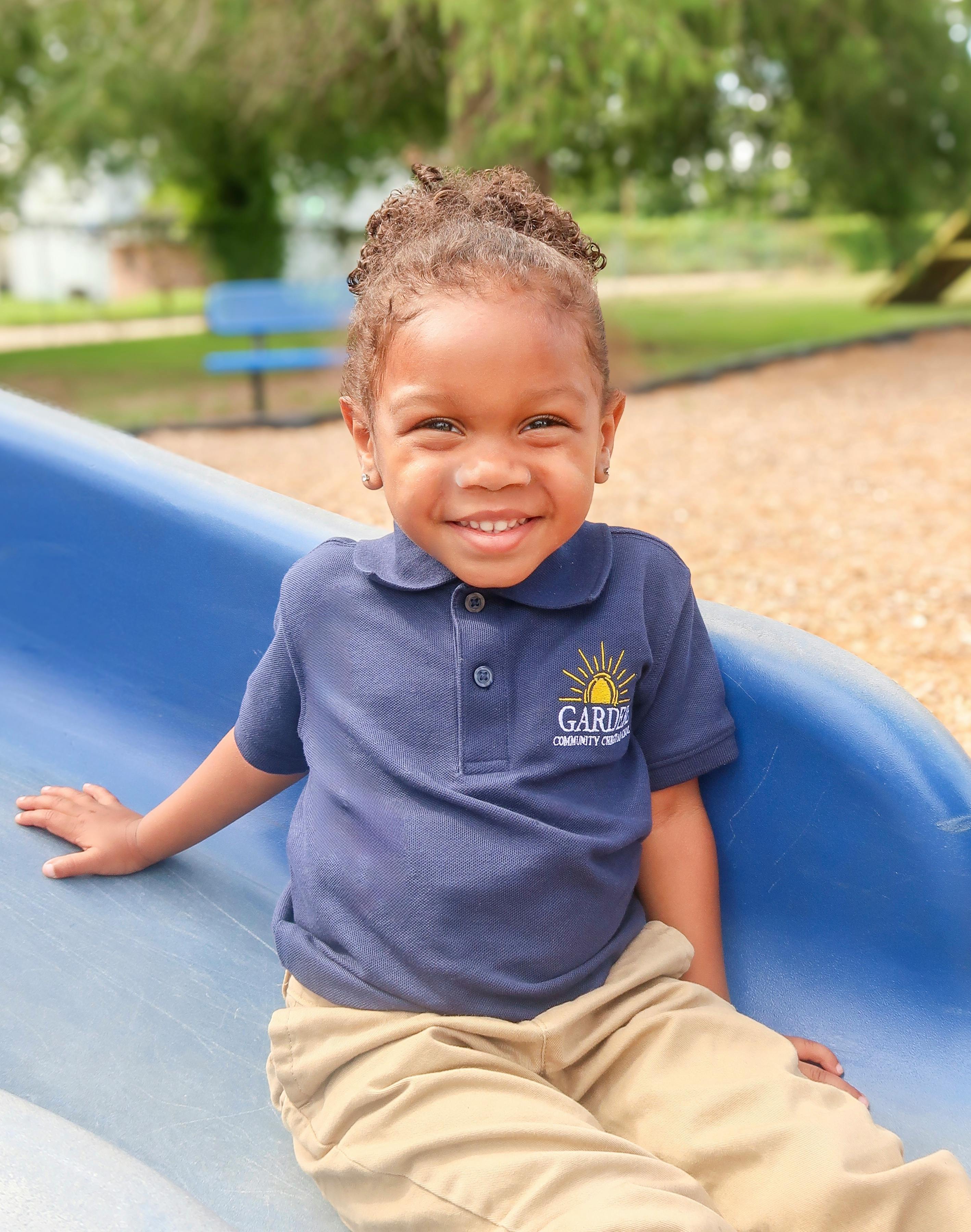 Child in a blue shirt and tan pants sitting on a blue slide