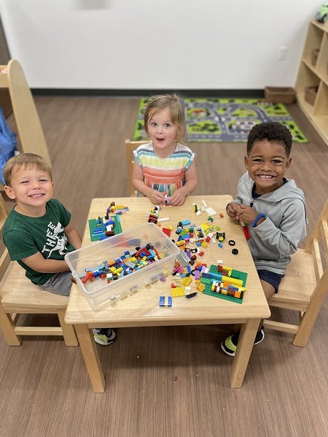 Three children playing with building blocks at a table