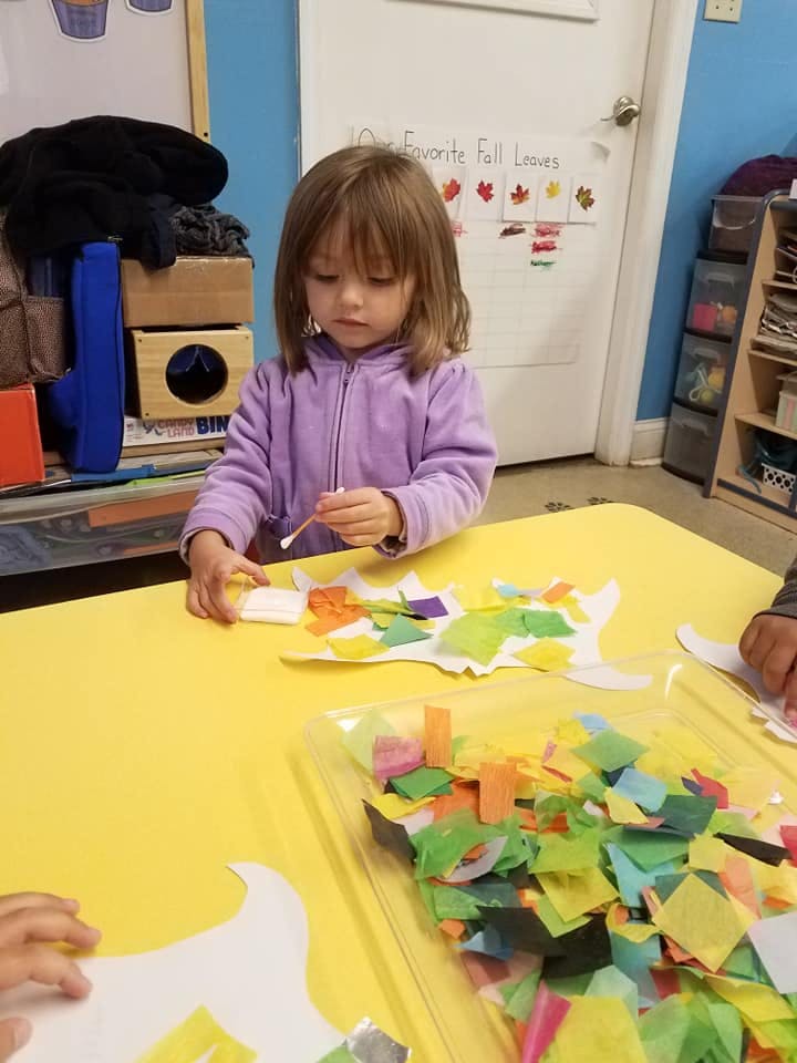 Child doing a craft with paper cutouts and a cotton swab at a table