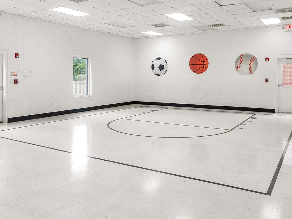 Indoor basketball court with large baseball, basketball, and soccer ball decals on the wall