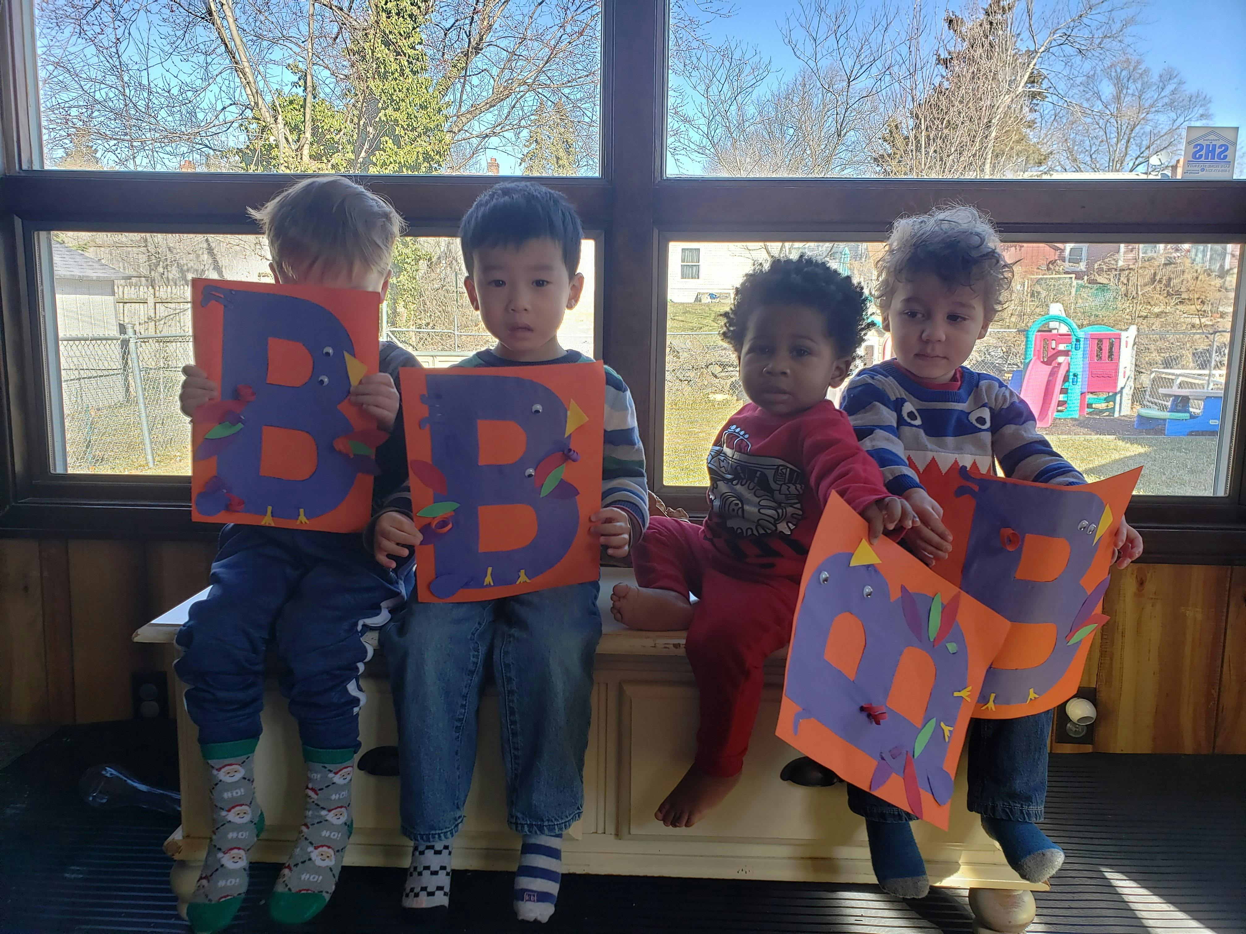 Four children holding orange papers with the letter B
