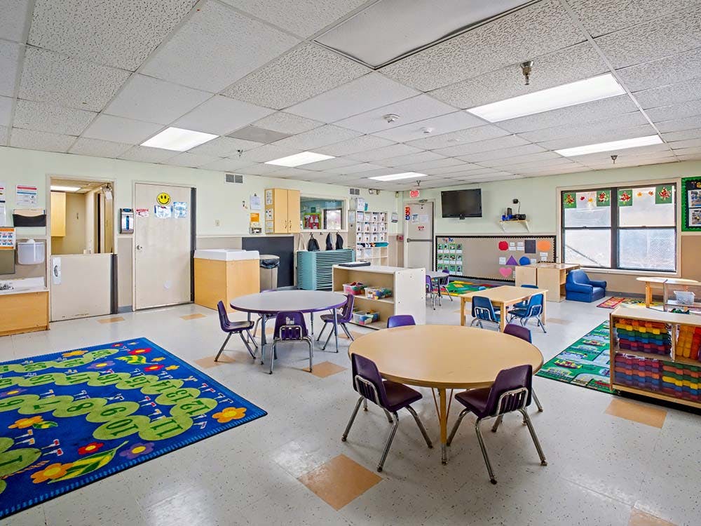 Classroom with small tables and chairs, shelves, and a rug with numbers