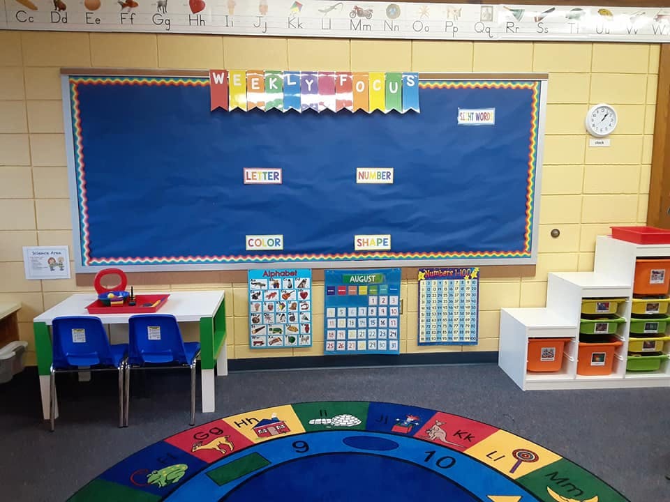 Classroom with a blue bulletin board, small table, and colorful rug