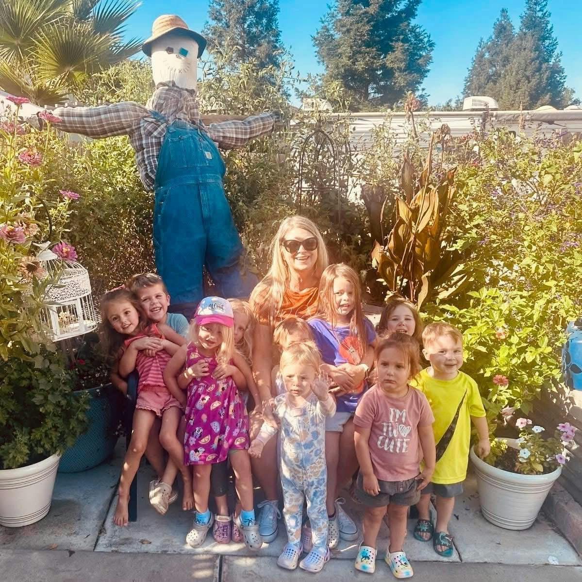 A group of children and a person posing next to a scarecrow in a garden