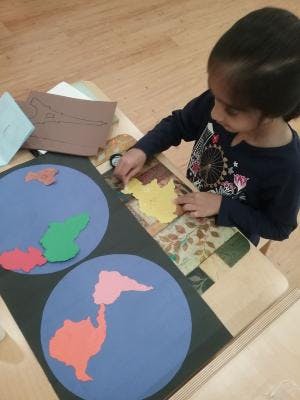 Child placing a yellow cutout shape on a blue circle with other shapes
