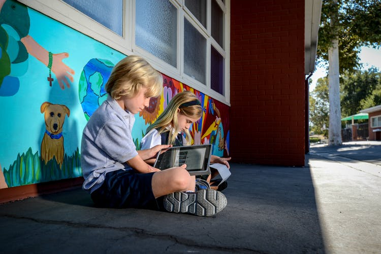 Two children sitting on the ground looking at a tablet