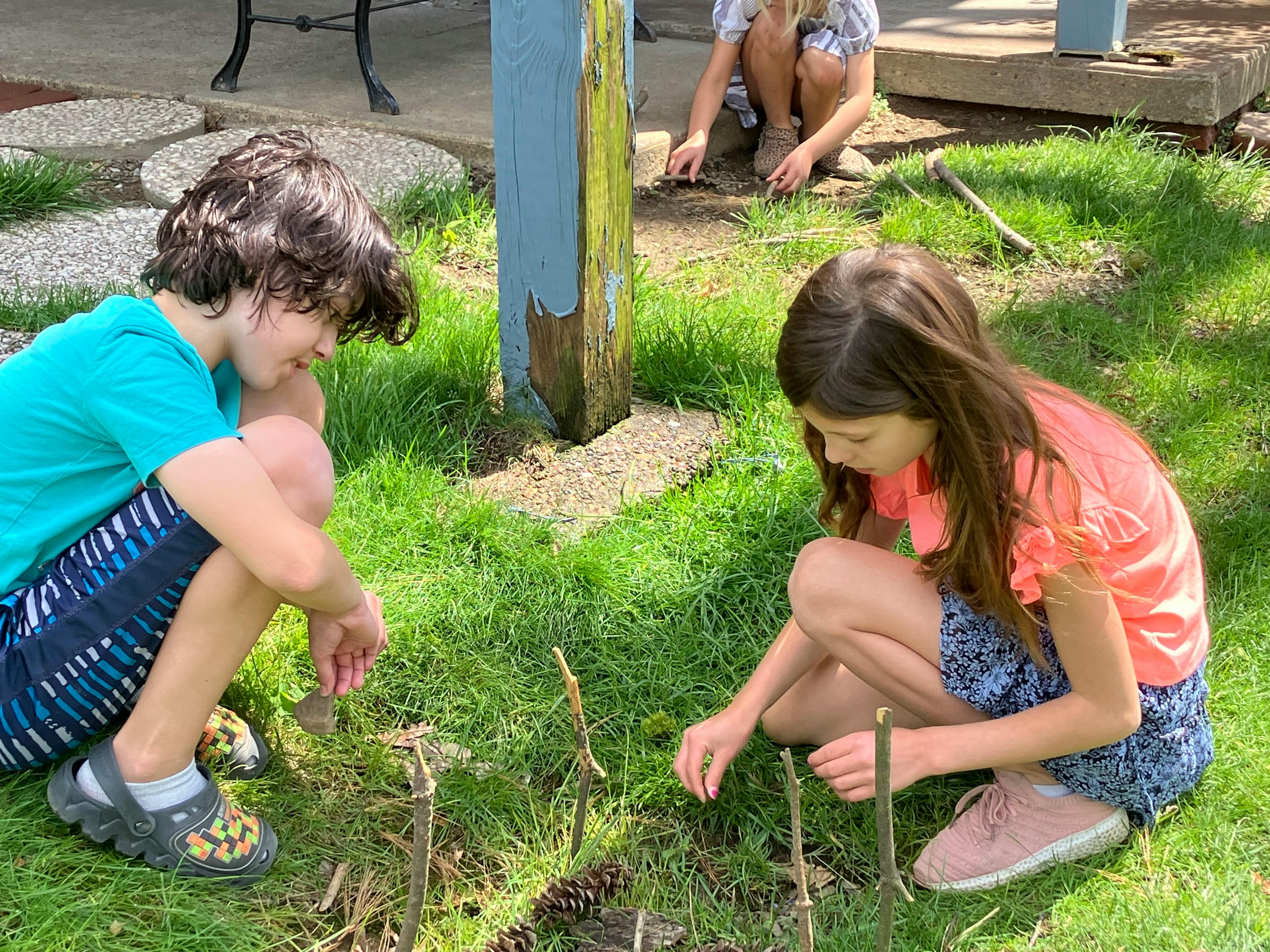 Children crouching in the grass playing with sticks and pinecones