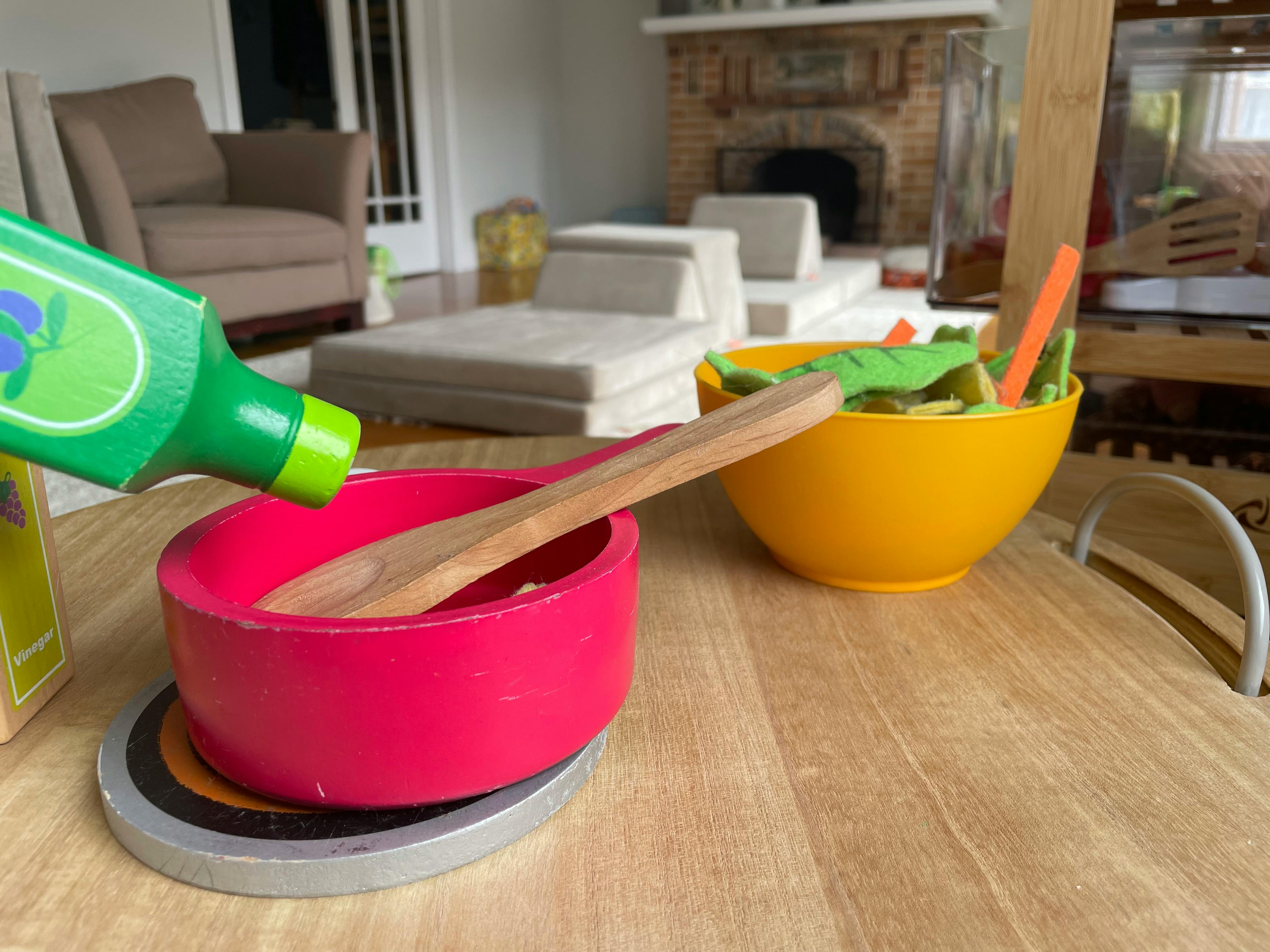 Toy cooking set with a green bottle, red pot, and yellow bowl of play food