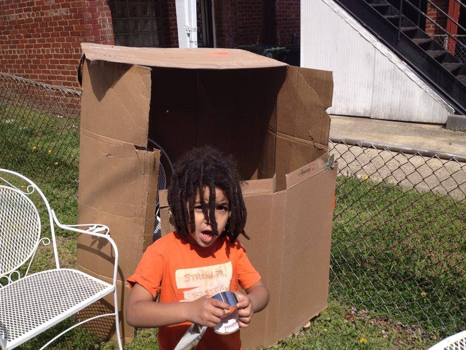 Child with dreadlocks standing in front of a large cardboard box