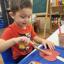 Child painting a red shape at a table