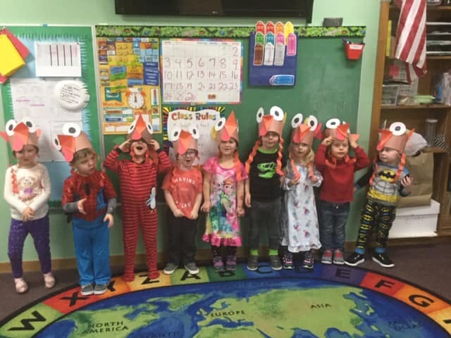 Children in a classroom wearing paper hats with googly eyes
